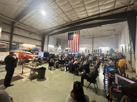 Man presents to seated audience in airplane hangar