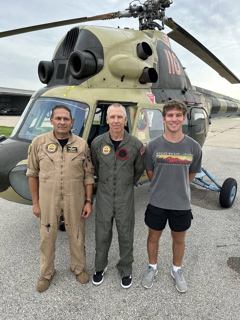 Three people pose for a photo in front of a helicopter