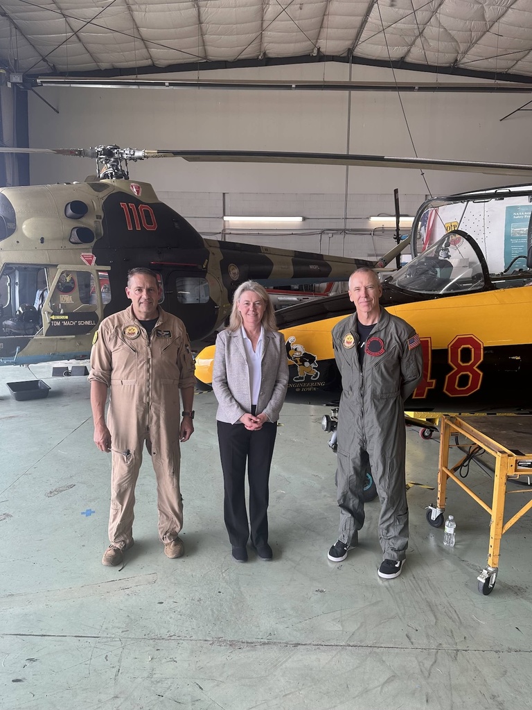 Three people pose for a photo in front of a helicopter