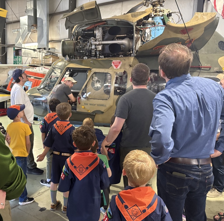 A group of adults and children crowd around a helicopter with camouflage paint