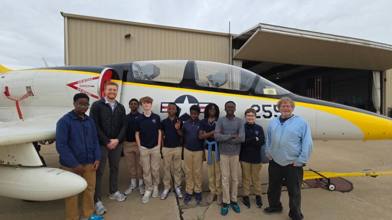 School group poses in front of jet