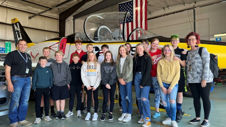 A group poses for a photo in front of a jet